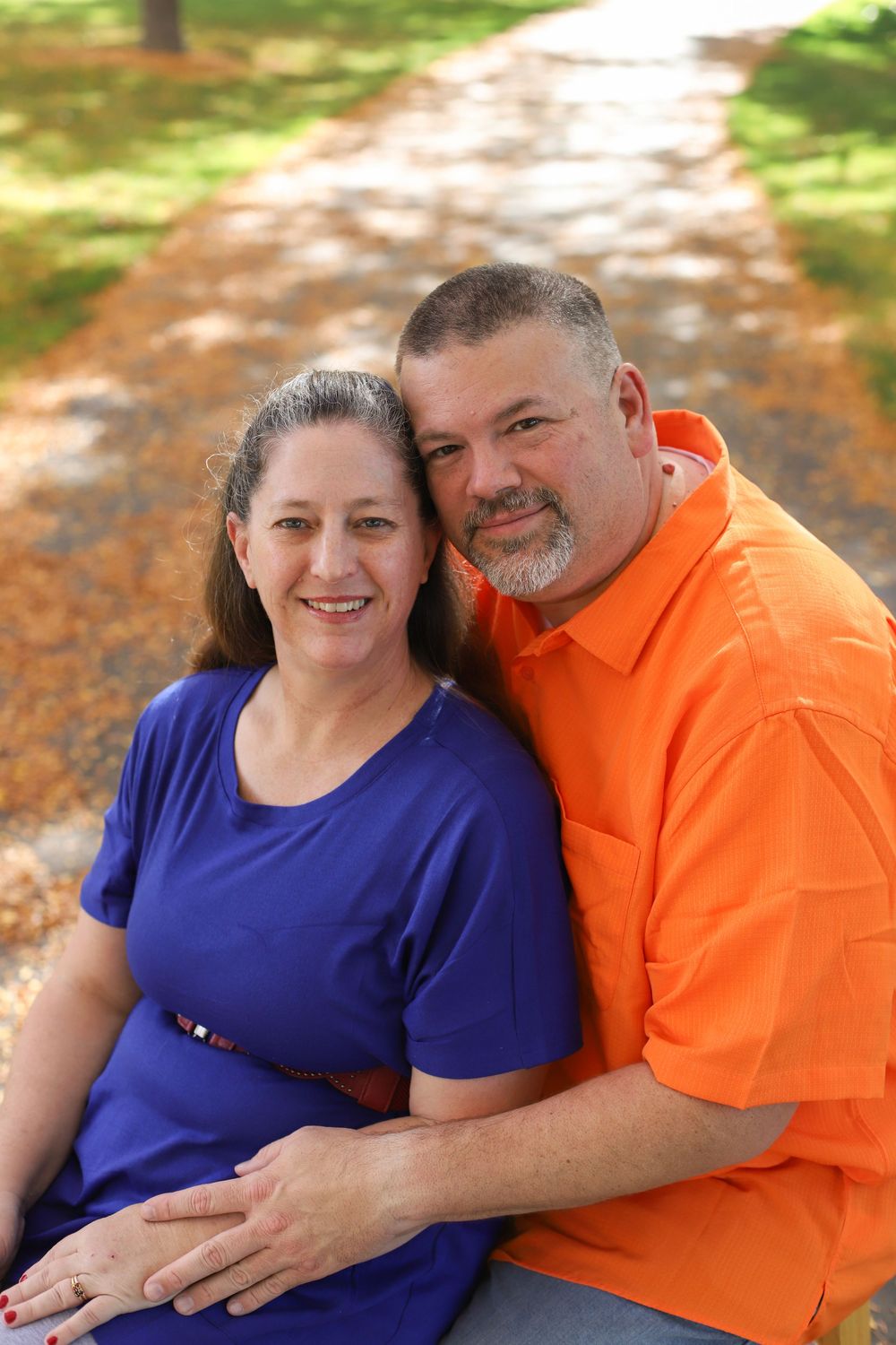 A couple wearing blue and orange shirts share affectionate moments in an outdoor autumn setting.