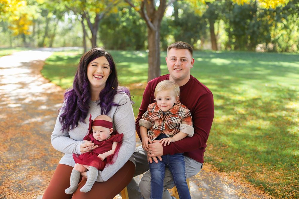 Family enjoying a fall photoshoot together on a path covered with autumn leaves in a sunlit park.