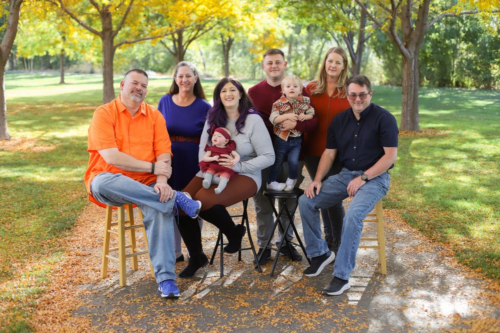 A group sits together on a rustic wooden bench in a sunlit autumn park surrounded by golden foliage.