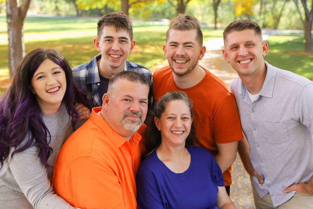 A cheerful group wearing orange and blue shirts poses together outdoors in a park on a sunny day.