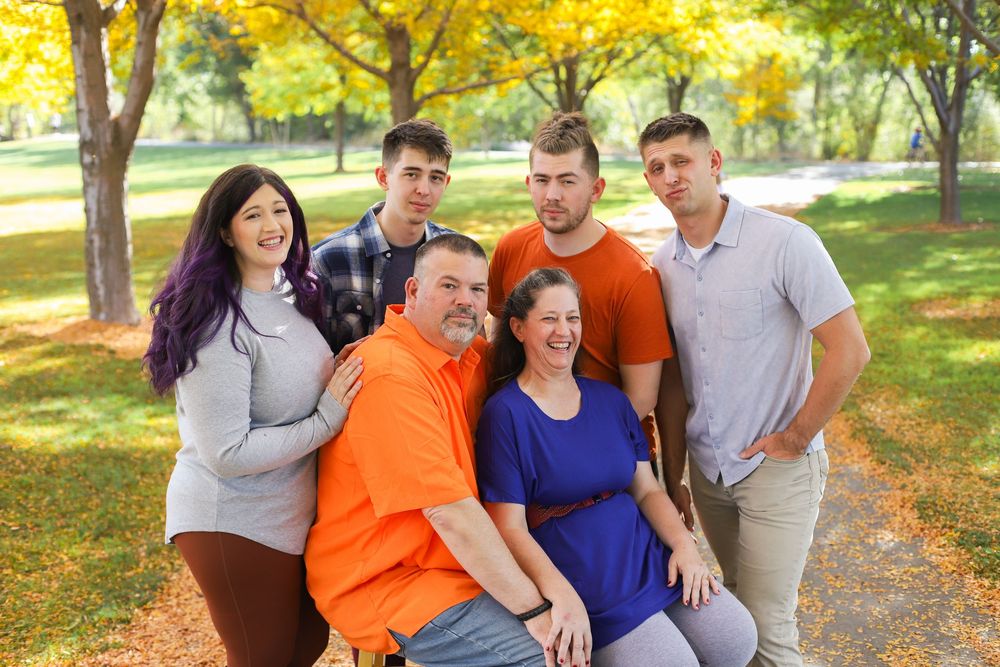 A group in orange and blue outfits poses together on a tree-lined path during autumn.