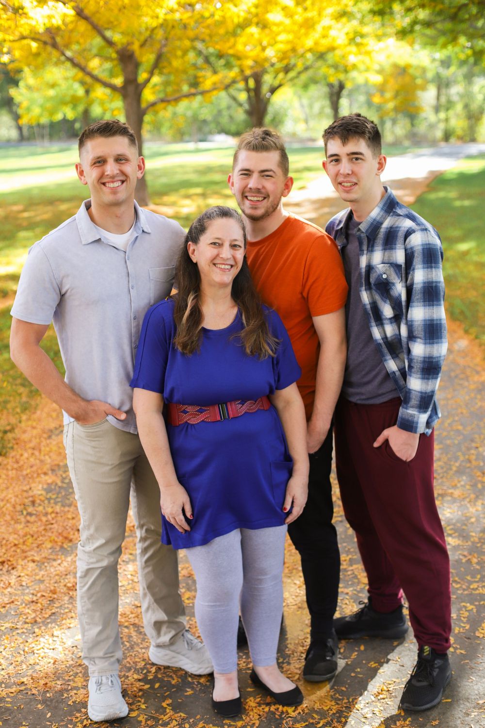 A group poses together outdoors in casual attire with autumn foliage creating a warm yellow backdrop in the background.
