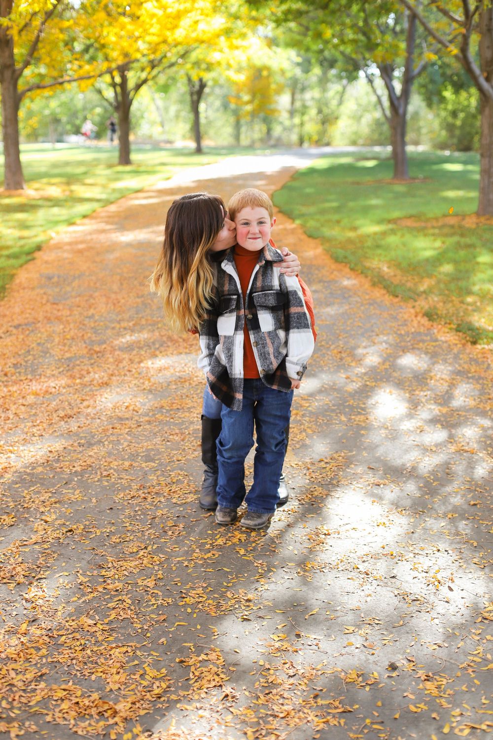 Small child walking on an autumn path covered in yellow and orange fallen leaves in a sunny park.