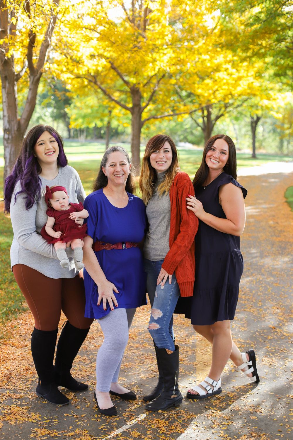 A group stands together on an autumn path with golden yellow foliage in the background during a fall photoshoot.
