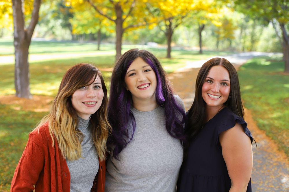 A group of friends smiling together while enjoying a sunny autumn day in a park with colorful fall foliage.