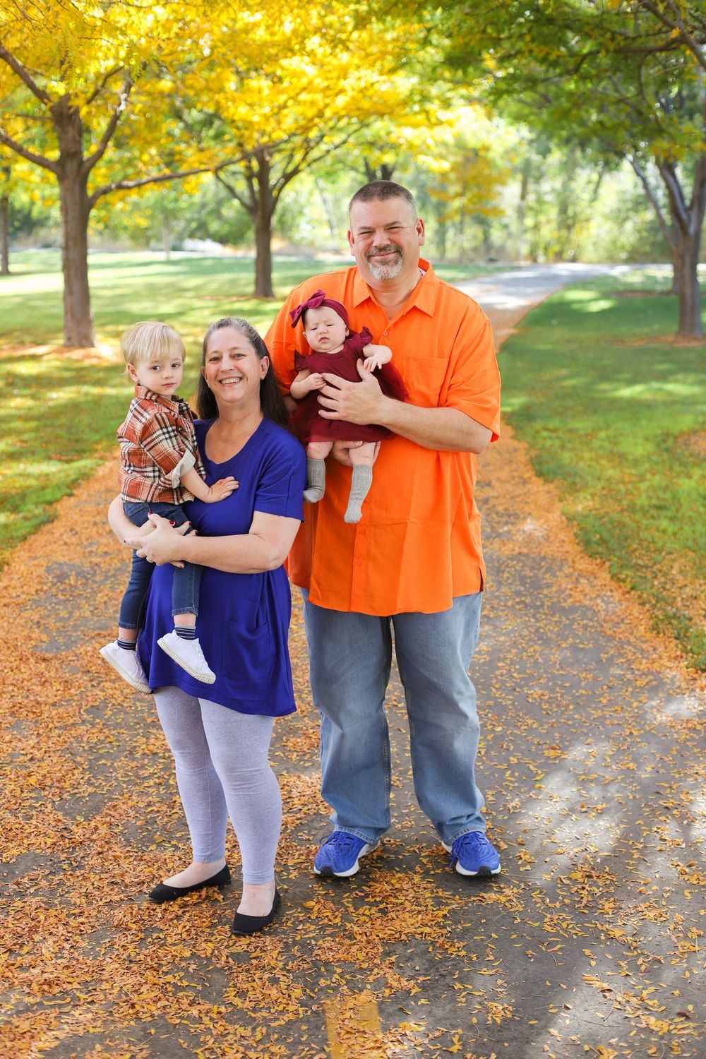 Family enjoying a fall day together on a leaf-covered path surrounded by golden autumn foliage.