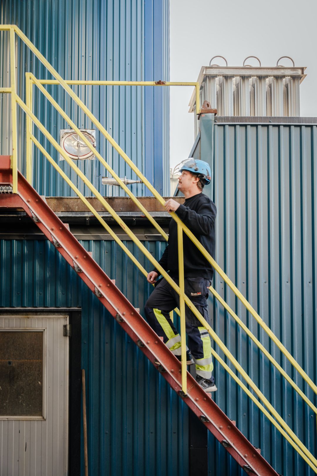 Man med skyddshjälm som går i trappa i industrimiljö. Företagsfotografering av Gabriel Alenius