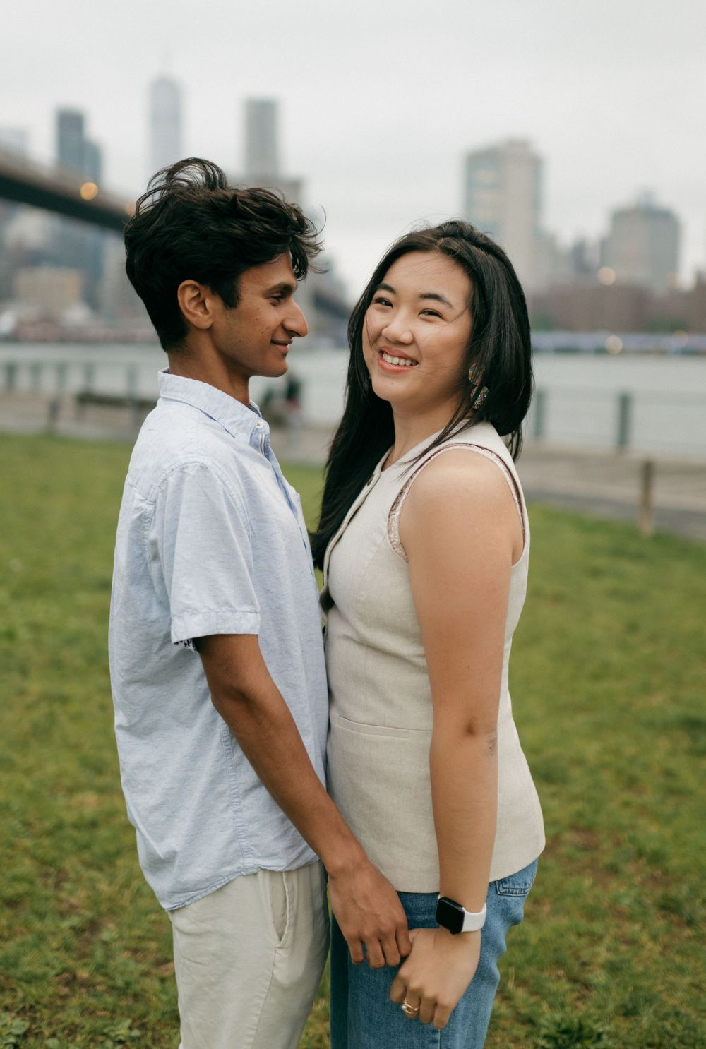 A couple shares tender moments together in a grassy field with a city skyline in the background.