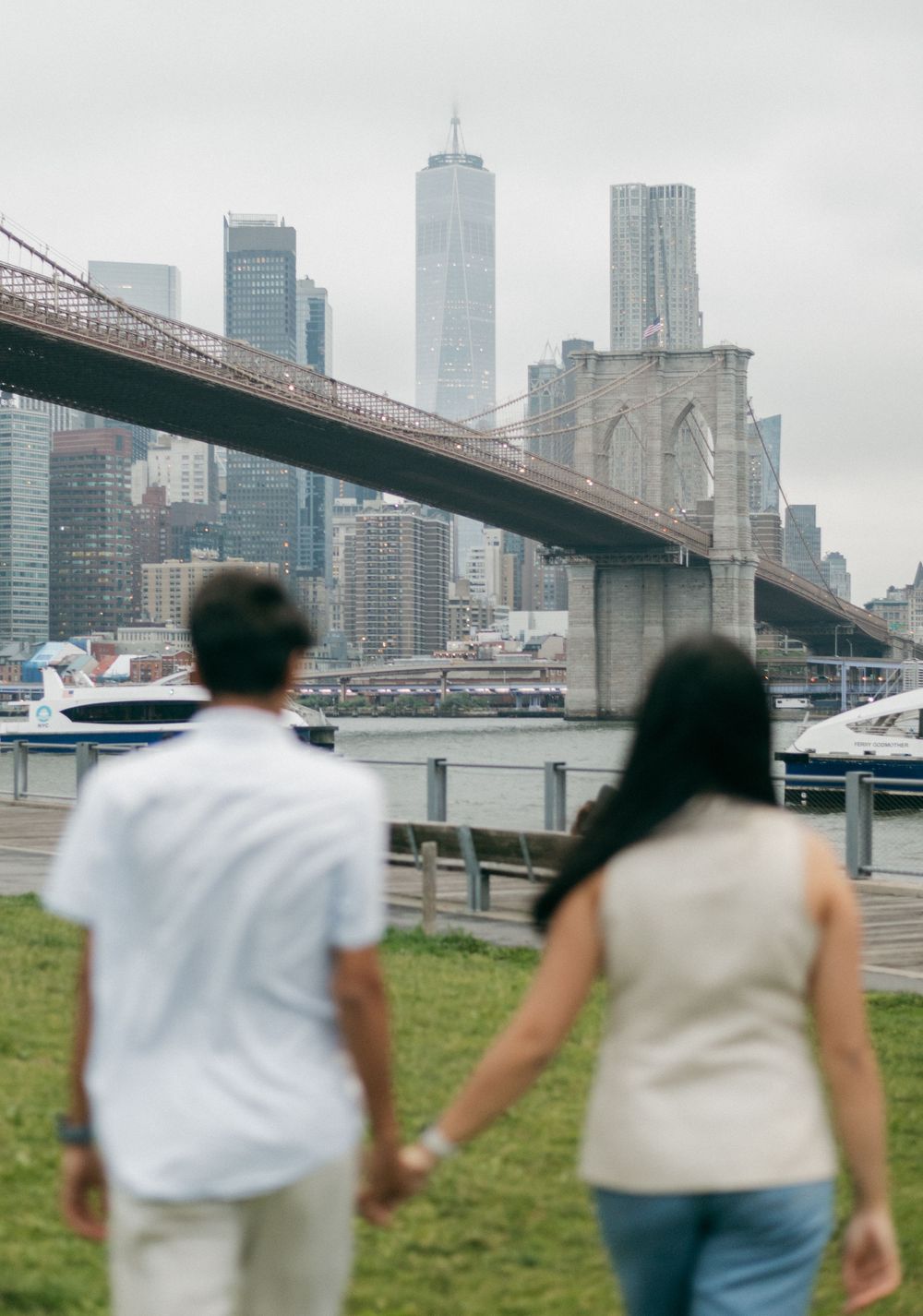 People walking near the Brooklyn Bridge with Manhattan skyline and tall skyscrapers visible in the background.
