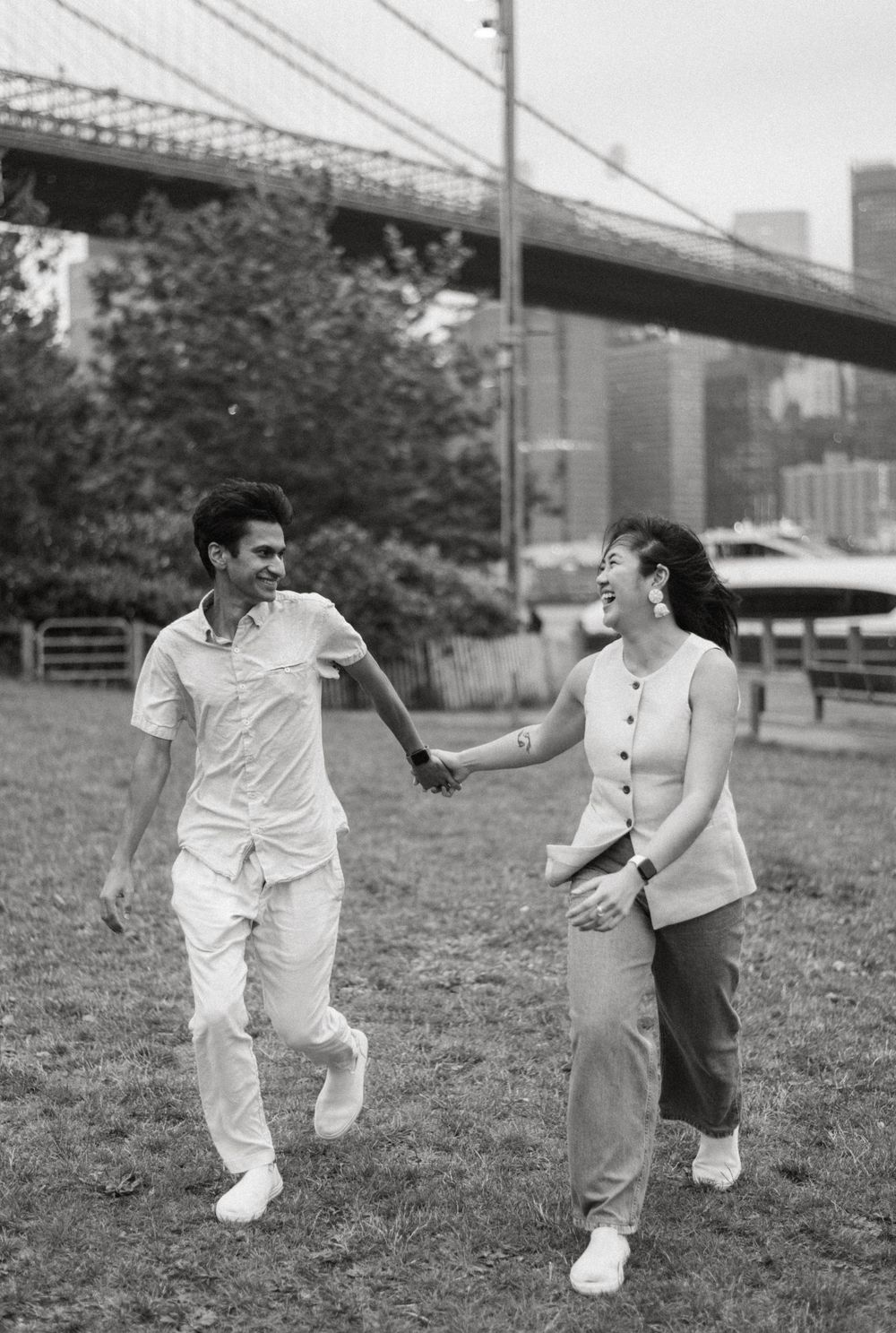 A couple dances playfully on grass near a bridge, captured in a sequence of black and white photographs.