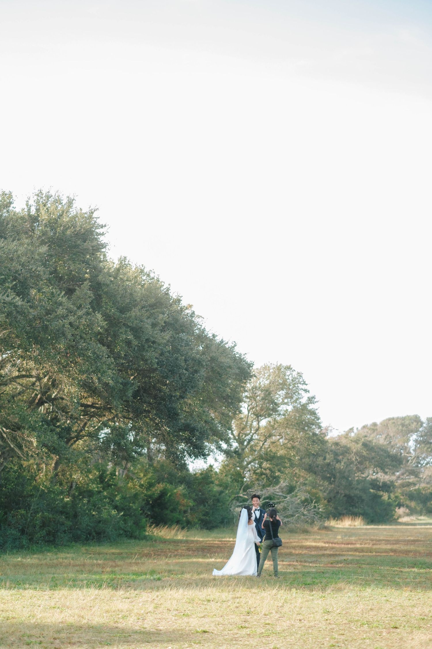 A couple walking together in a serene meadow surrounded by trees during golden hour.