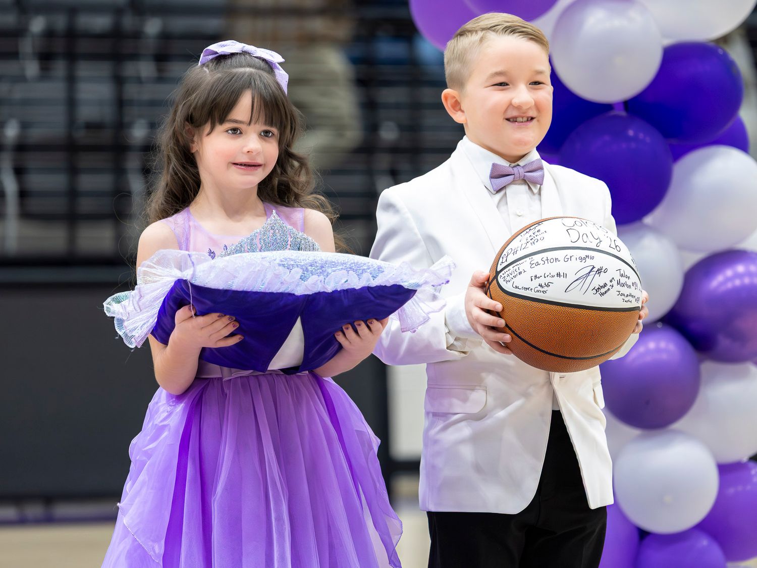 A group in purple and white attire performs with books in front of balloon decorations.