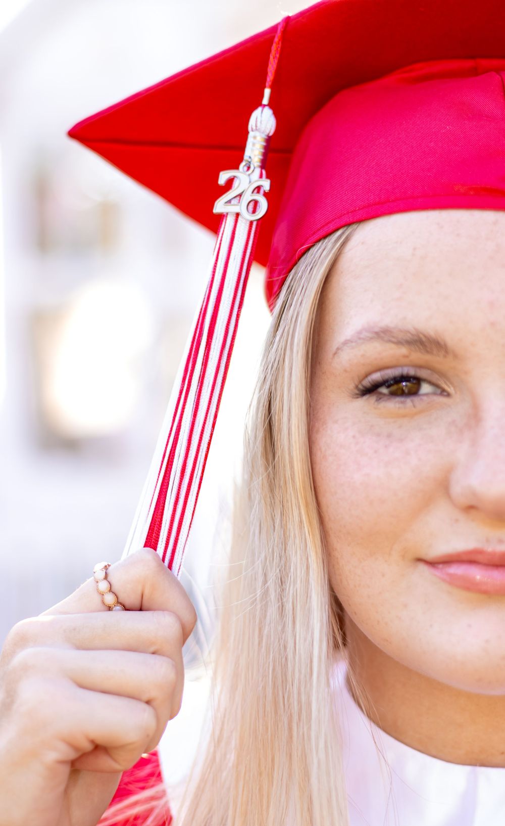 Graduate wearing red cap and gown holds white and red tassel while posing for graduation photo.