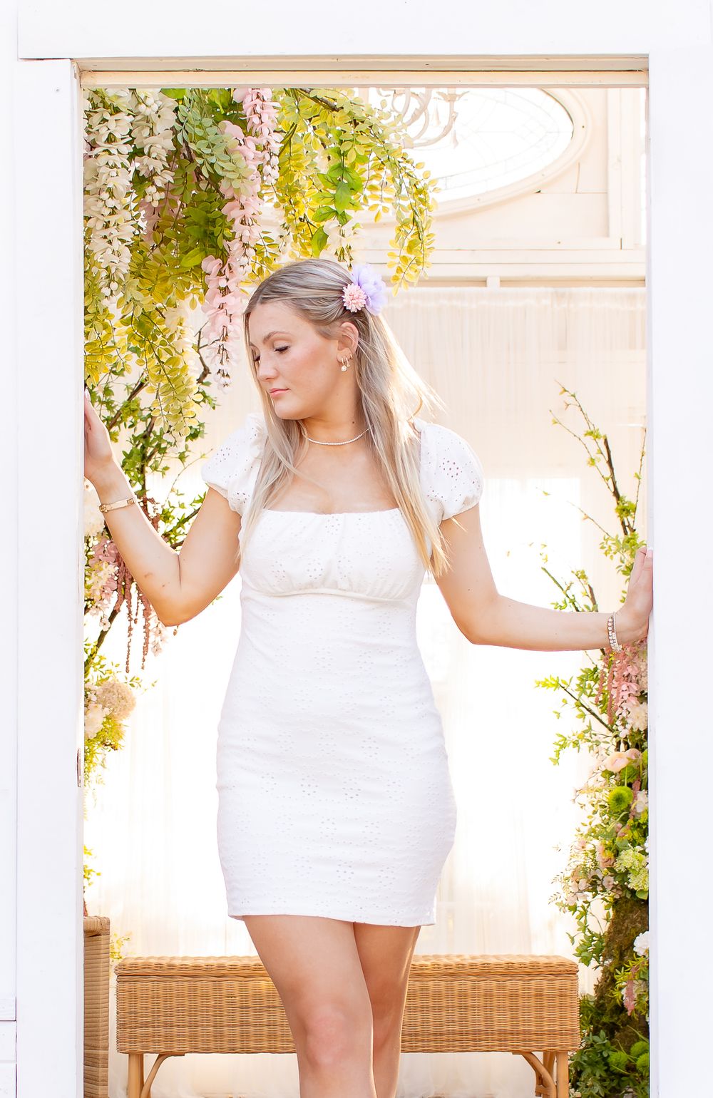 A person in a white dress poses near a window with hanging vines and natural light creating a romantic atmosphere.