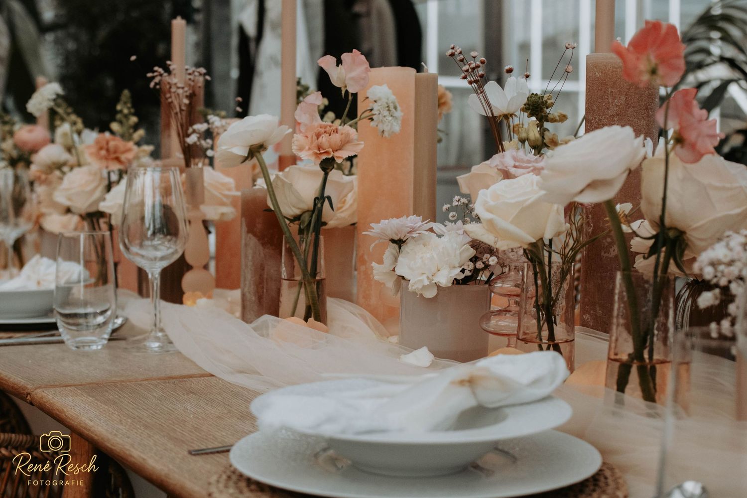 Elegant wedding table setting with white and pink floral arrangements, rose gold accents, and neatly folded napkins on white plates.