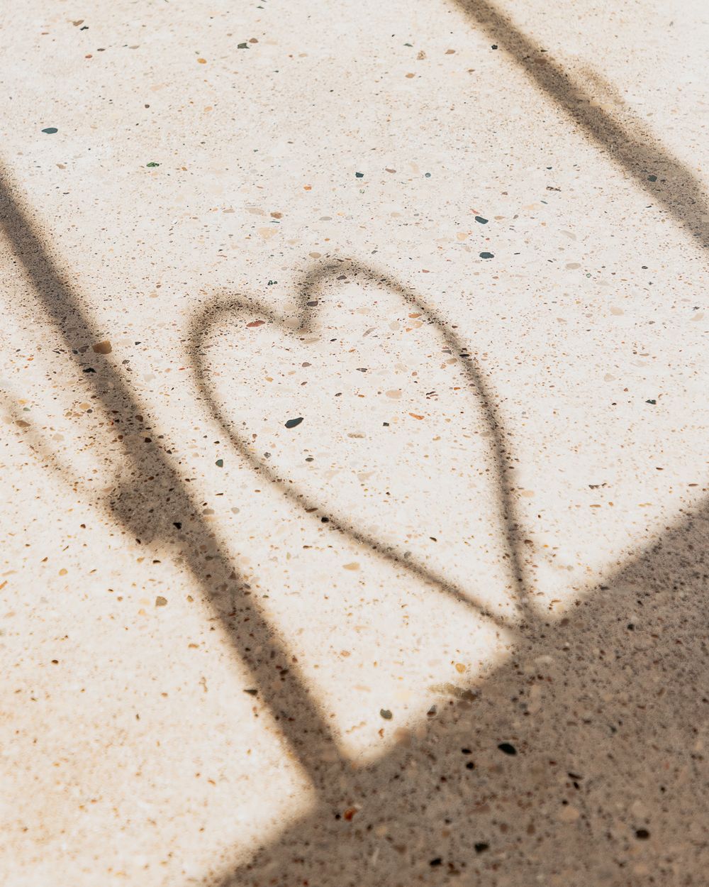 Shadow of a heart shape cast on sandy concrete surface in warm sunlight.