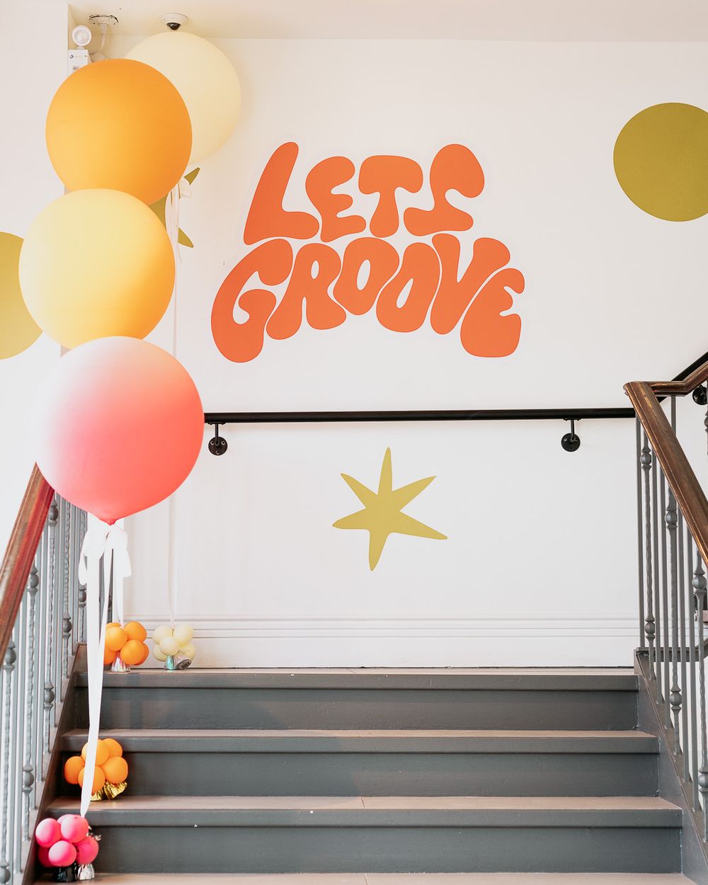 Retro staircase decorated with colorful balloons and a bold orange 'Let's Groove' wall mural with gold star accents.