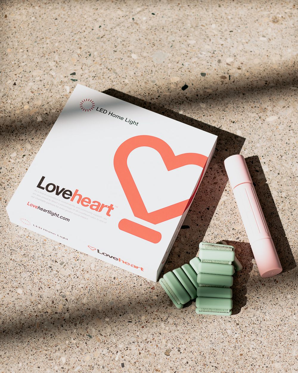Loveheart LED Home Light product box with green accessories and pink pen on sandy surface.