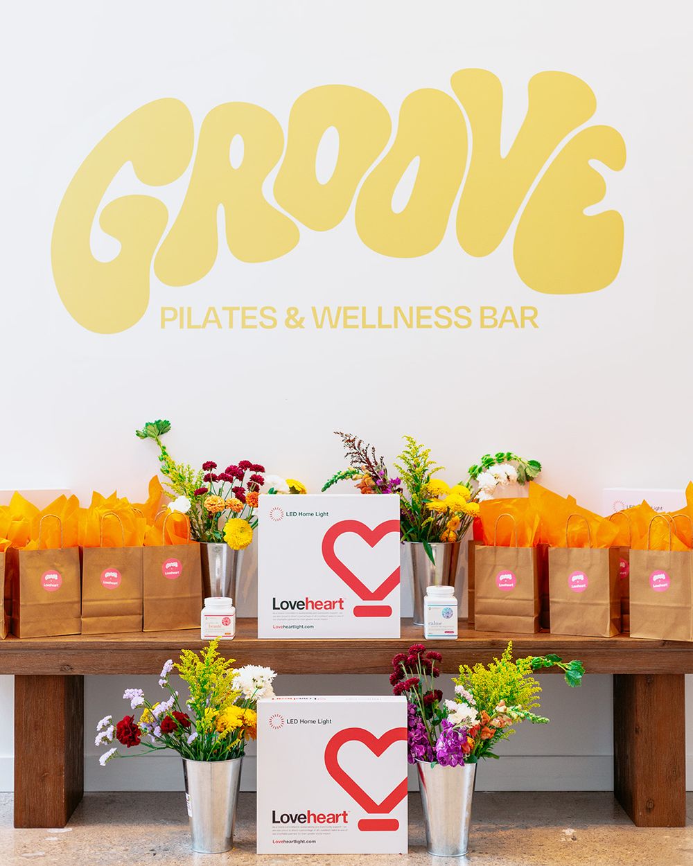 Groove Pilates & Wellness Bar display table with Loveheart boxes, orange gift bags, and colorful flowers.