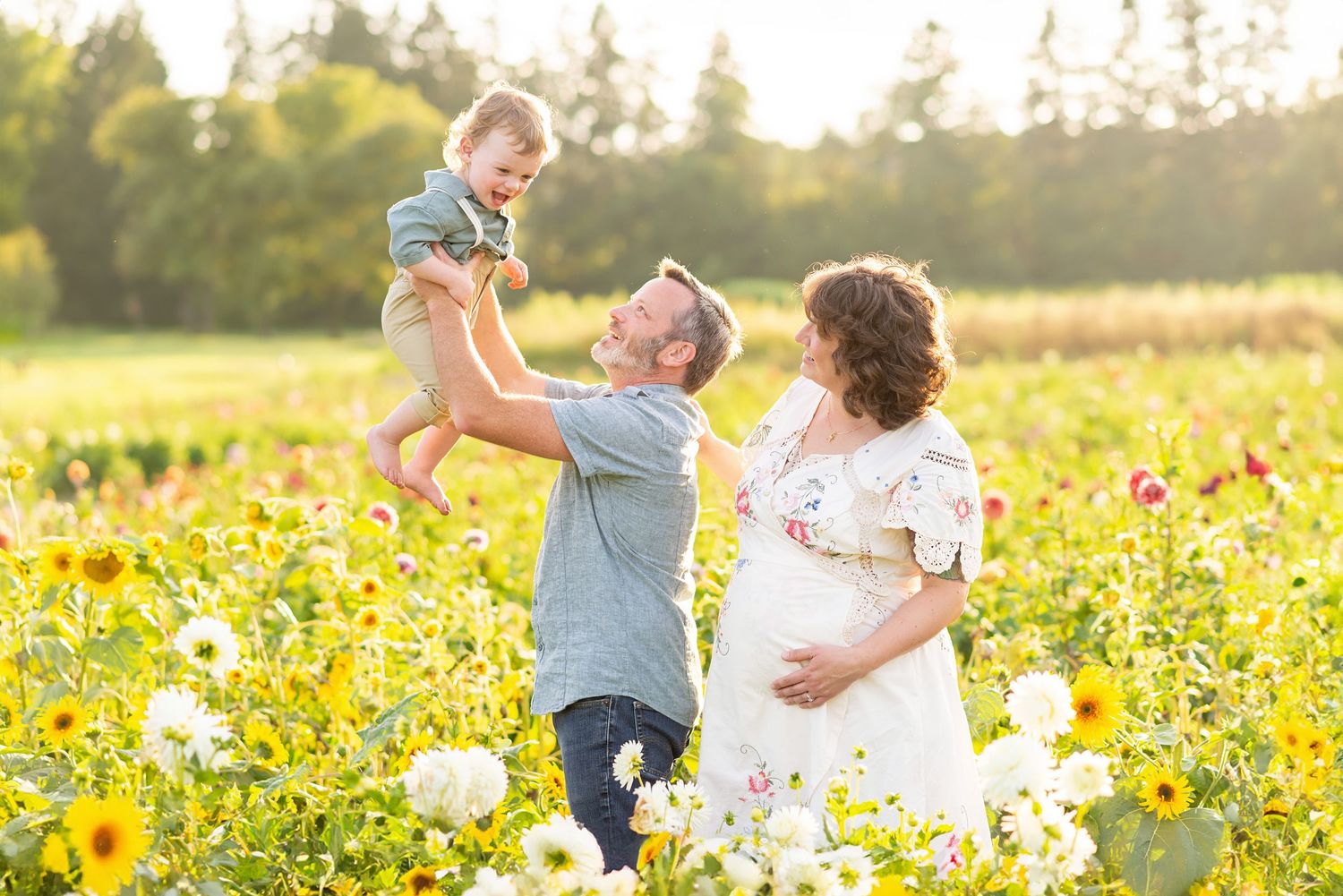 Pregnant woman in white dress with husband and toddler in sunny flower field maternity photo session at the Flower lady and Gent.