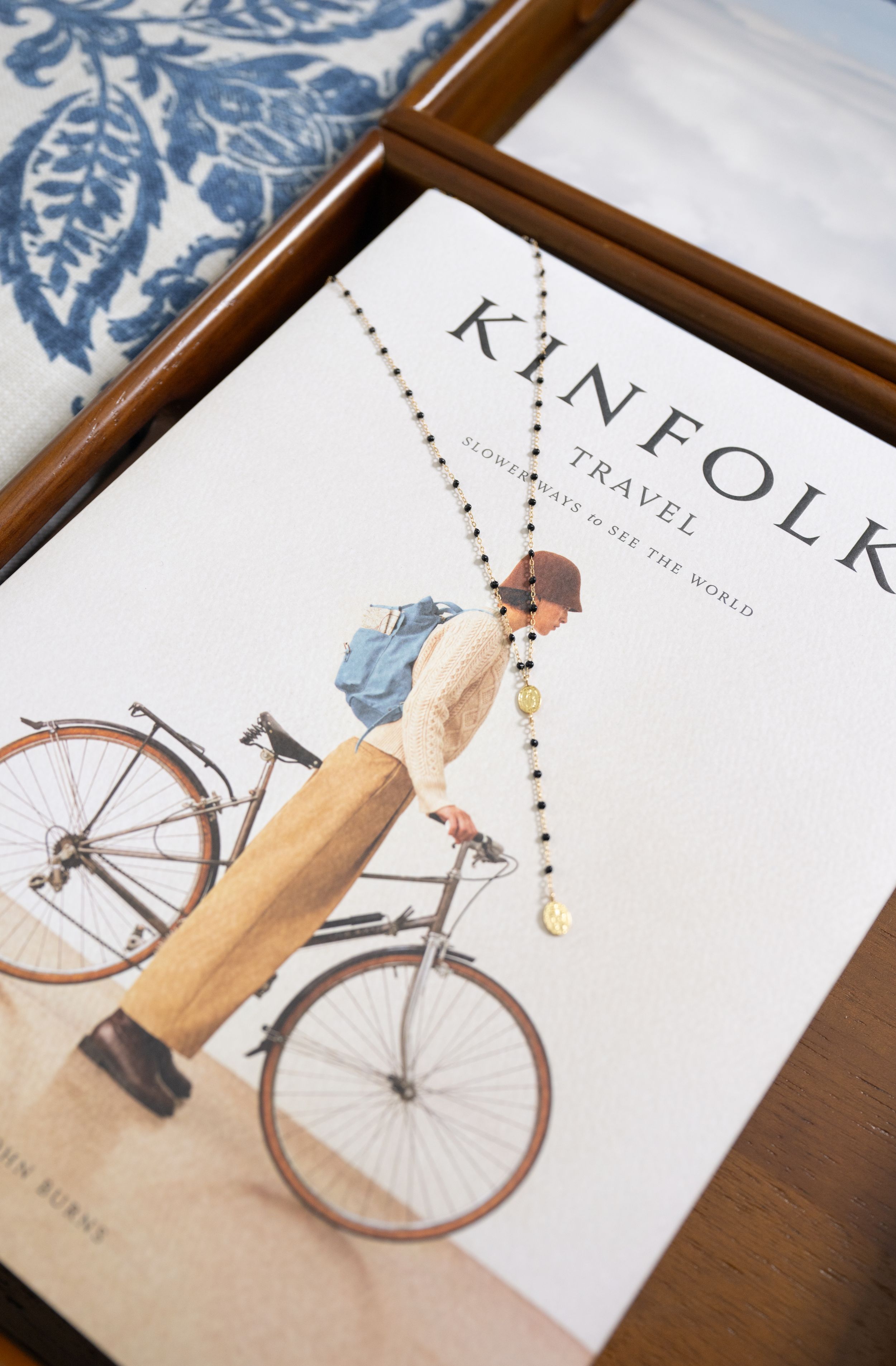 Kinfolk Travel book with a beaded necklace draped on the cover, featuring a person with a bicycle illustration.