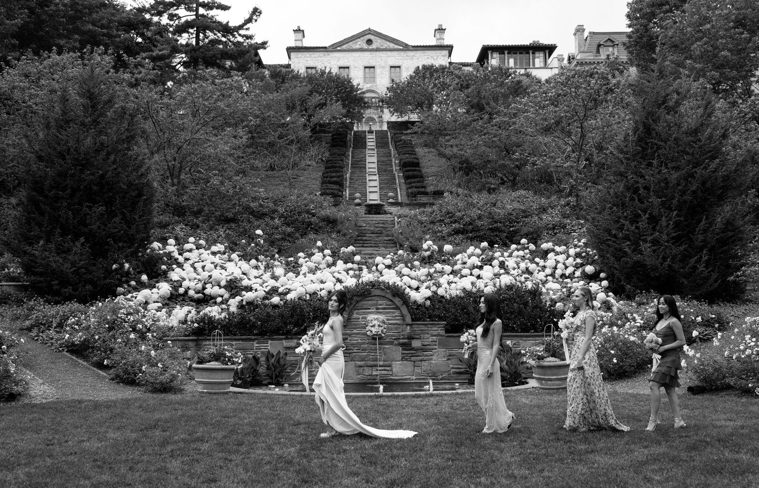 Editorial wedding photo at The Villa Terrace of a bride and bridesmaids in a formal garden with grand staircase and blooming roses.