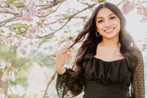 Young woman in black off-shoulder dress smiling under pink cherry blossom trees in spring in Lake Junaluska NC