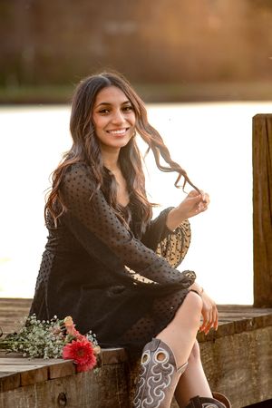 Young woman in black lace dress and cowboy boots sitting on wooden dock by lake at golden hour at Lake Junaluska