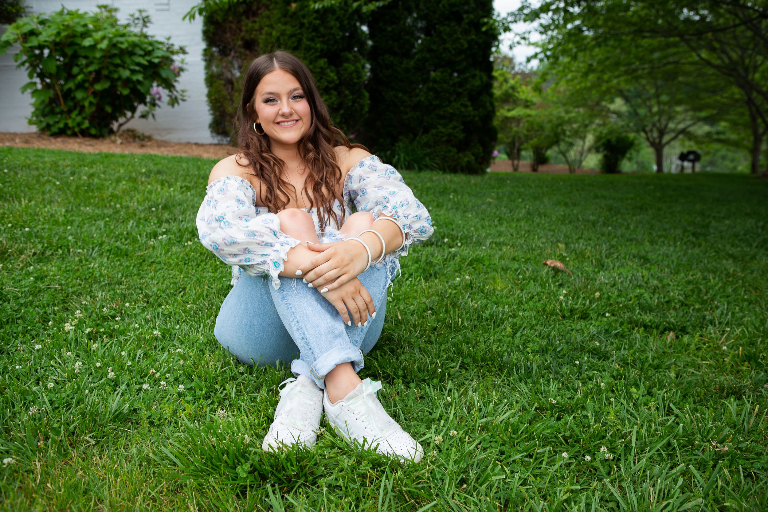 Young woman in white floral top and jeans sitting outdoors, smiling and posing for a portrait photo at Jackson County Public courthouse NC