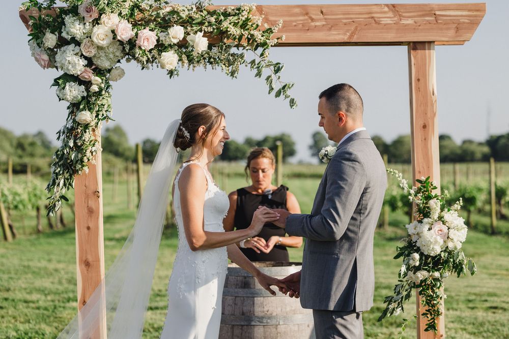 A couple shares their first look moment under a rustic wooden arch decorated with white flowers and greenery.