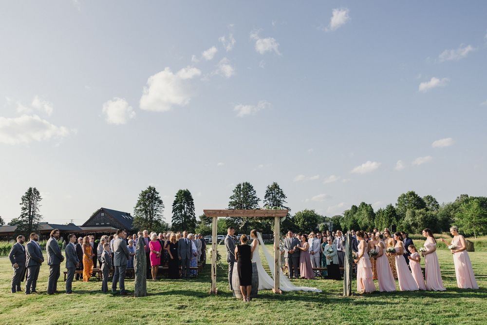 Panoramic view of wedding celebration in outdoor venue with guests lined up against blue sky backdrop.