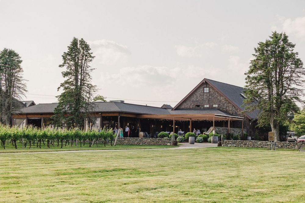 A panoramic view of a rustic barn and farmhouse complex surrounded by green pastures and tall trees.