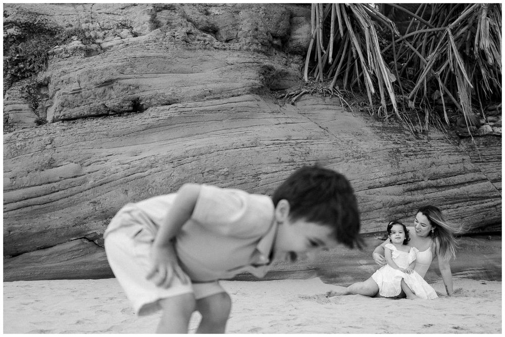 A black and white photograph showing someone bending down near a toy on rocky terrain.
