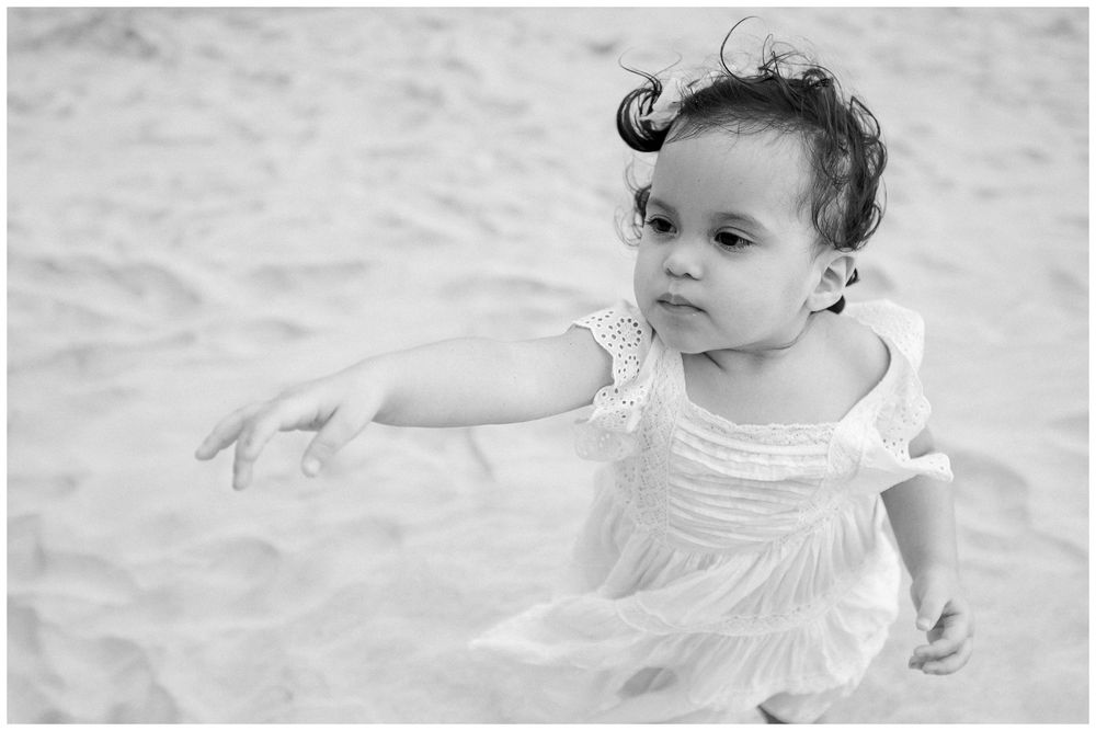 Black and white photo of a baby wearing a white dress crawling on a textured surface.