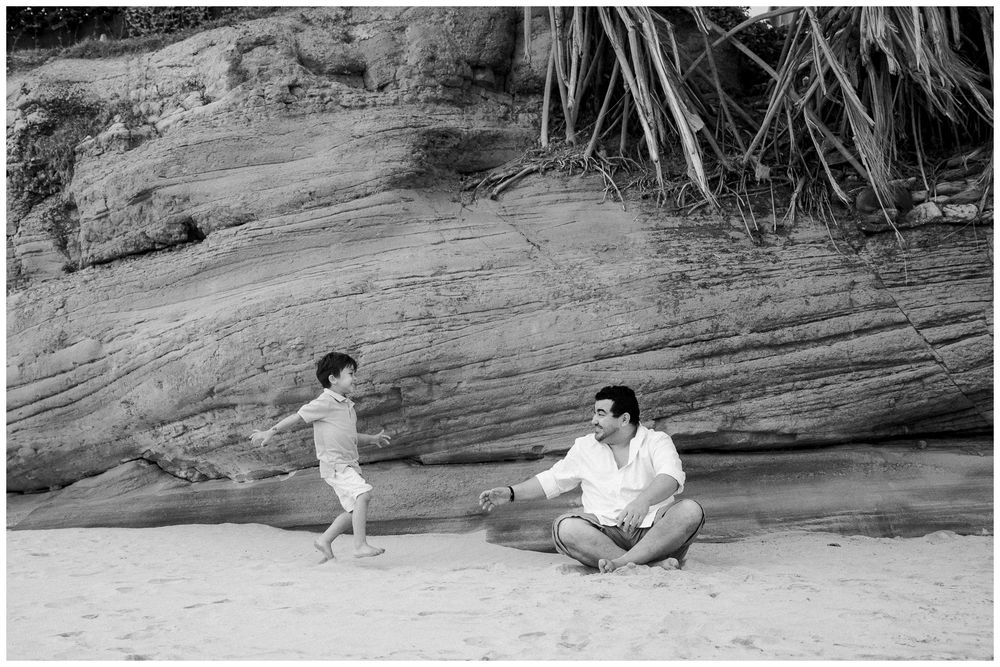 Two people play together on a rocky slope near water, creating a playful outdoor scene.