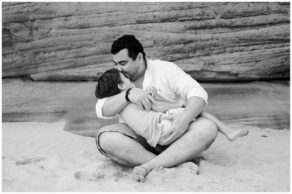 A series of black and white photos showing two people lying close together on a sandy beach near rock formations.