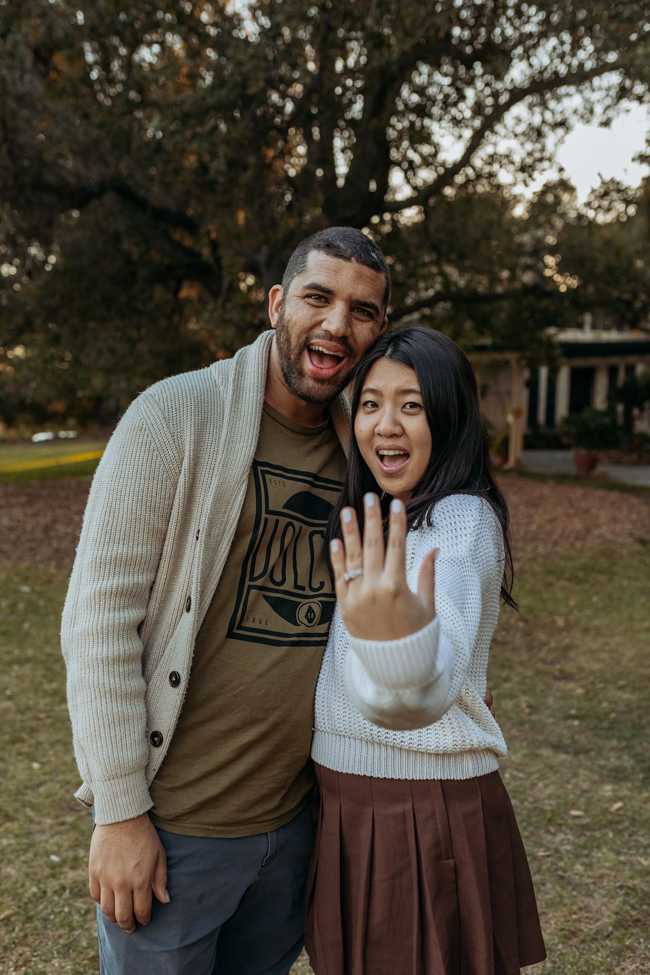 A couple shares joyful moments together in an outdoor Winter setting with fallen leaves and trees in the background.
