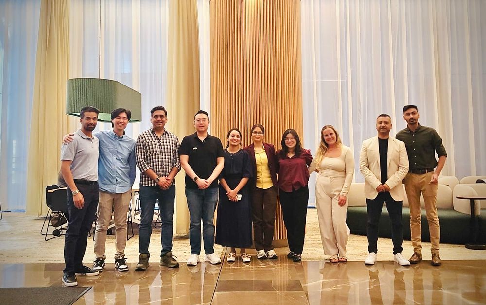 Group of ten smiling professionals standing together in a stylish hotel lobby setting.