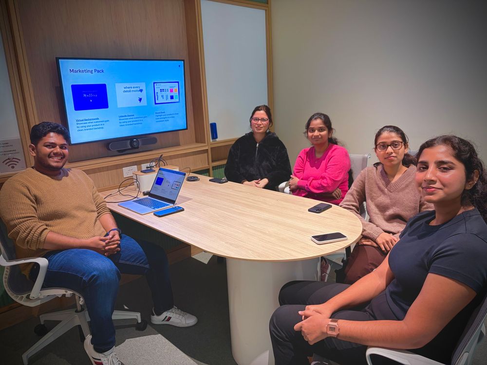Five professionals collaborate in a modern conference room with a presentation displayed on a large screen behind them.