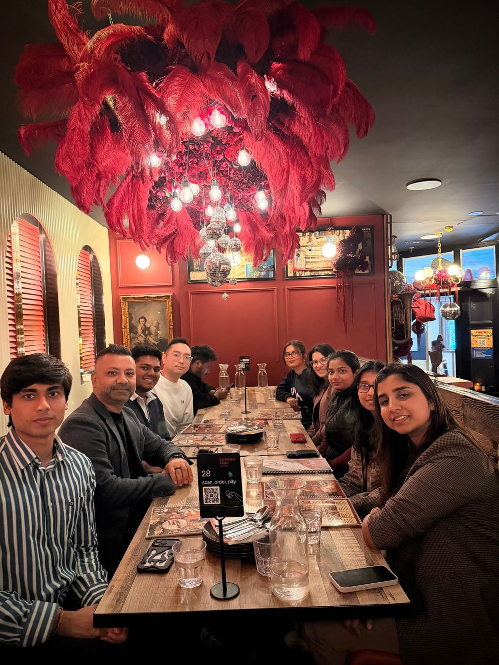 Group of friends dining at a vibrant restaurant with red feather chandelier and warm ambiance.