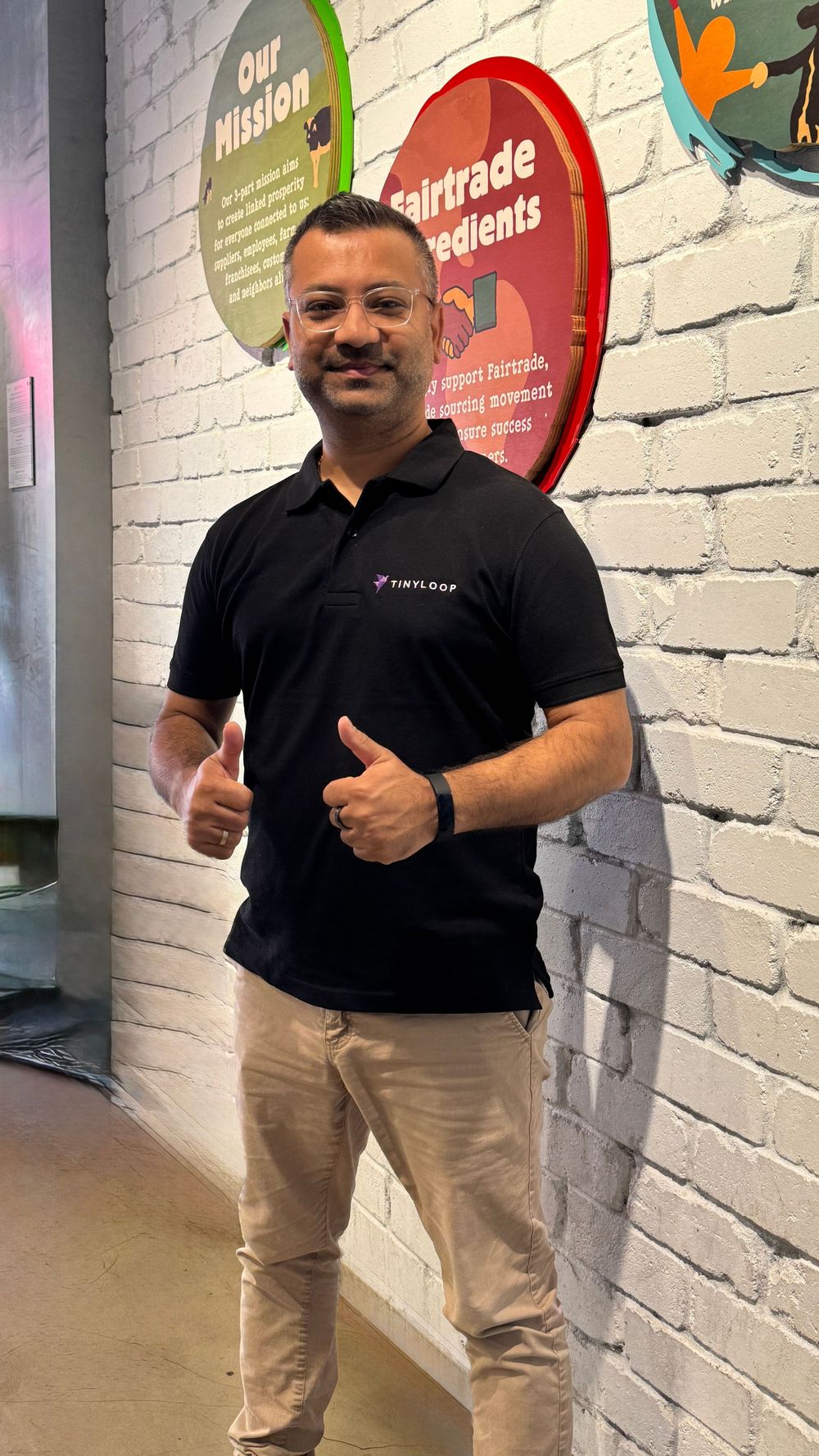Man in black TinyLoop polo shirt giving thumbs up inside a colorful retail store.