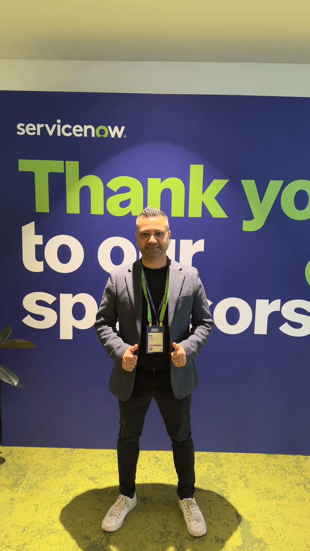 Man posing confidently in front of a ServiceNow thank you sponsors banner at a conference.