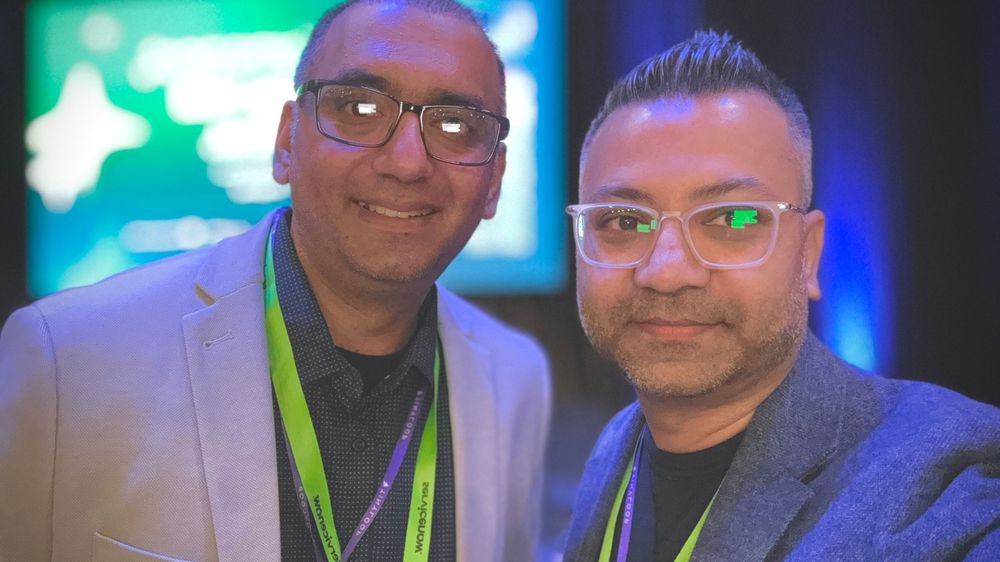 Two smiling men wearing event lanyards posing together at a professional conference.
