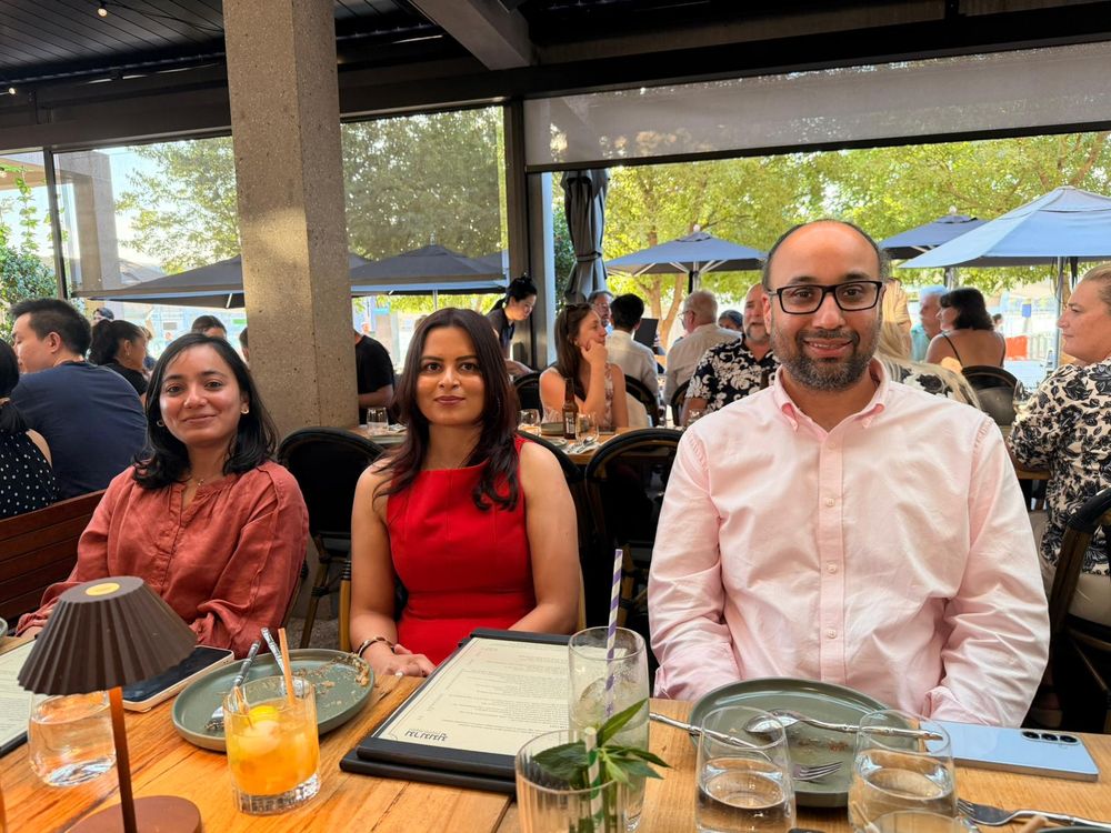 Three colleagues smiling at a restaurant table with colorful drinks.