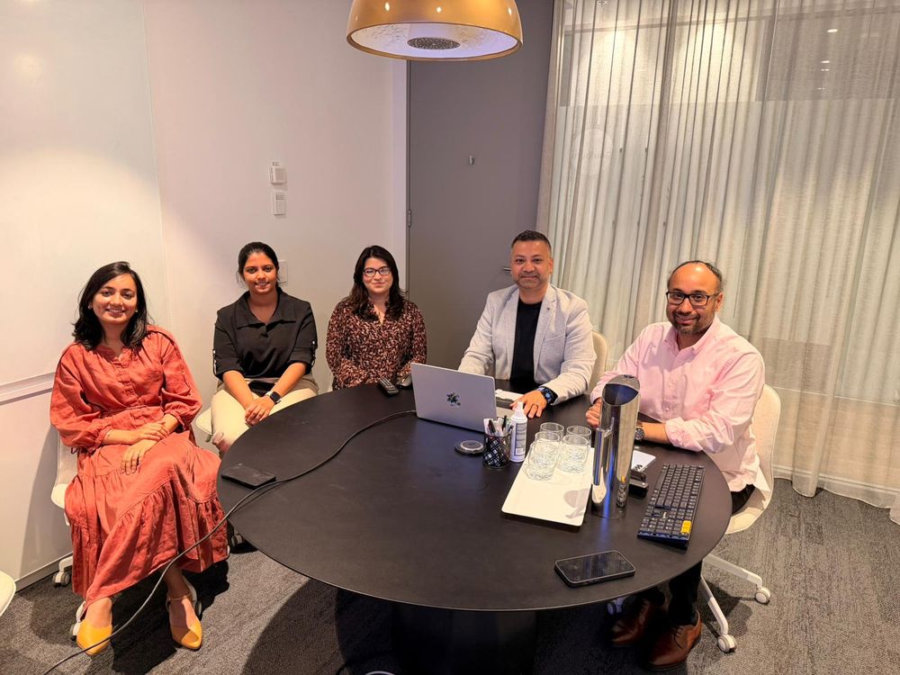 Five professionals in a modern meeting room gathered around a conference table.