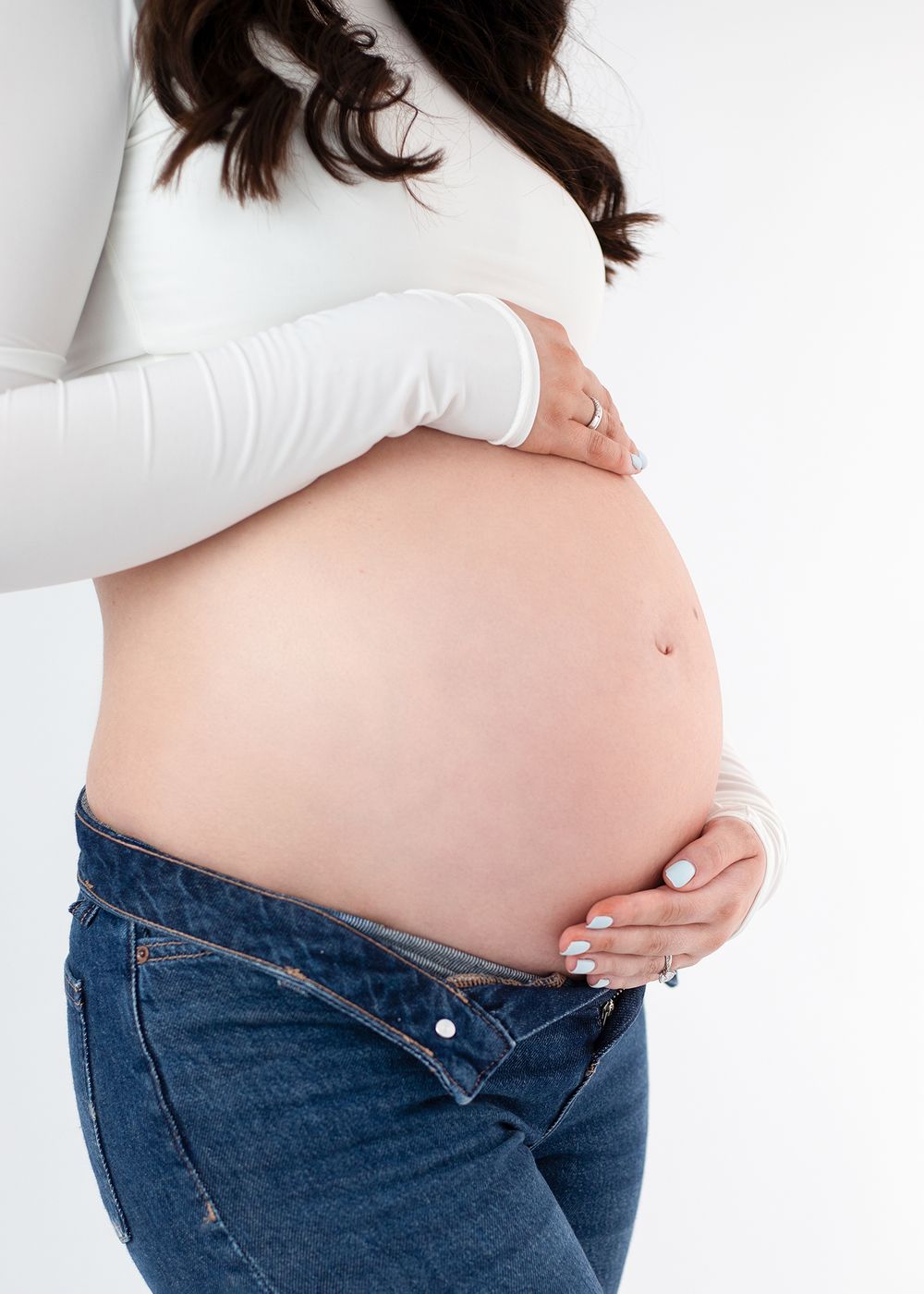 Four side-by-side photos showing a pregnant woman's growing belly in jeans and white top against a white background.