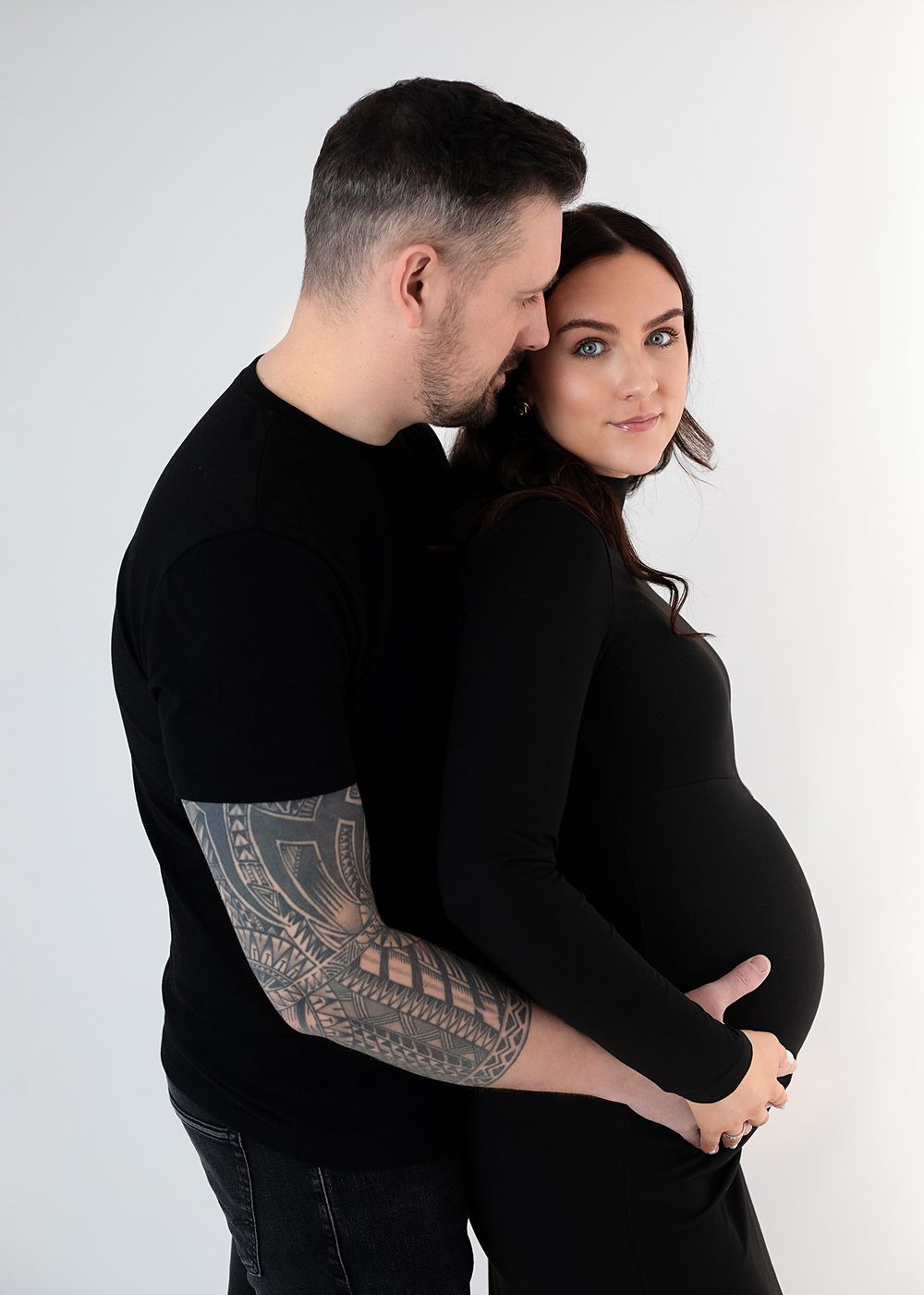 A couple in black clothing embraces tenderly against a white background in a series of intimate poses.