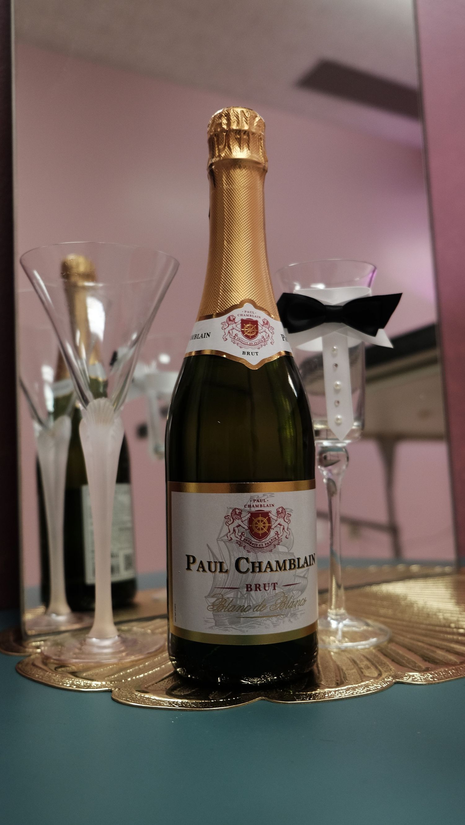 Paul Chamblain Brut champagne bottle beside two elegant flutes with bow tie decoration on a gold tray.
