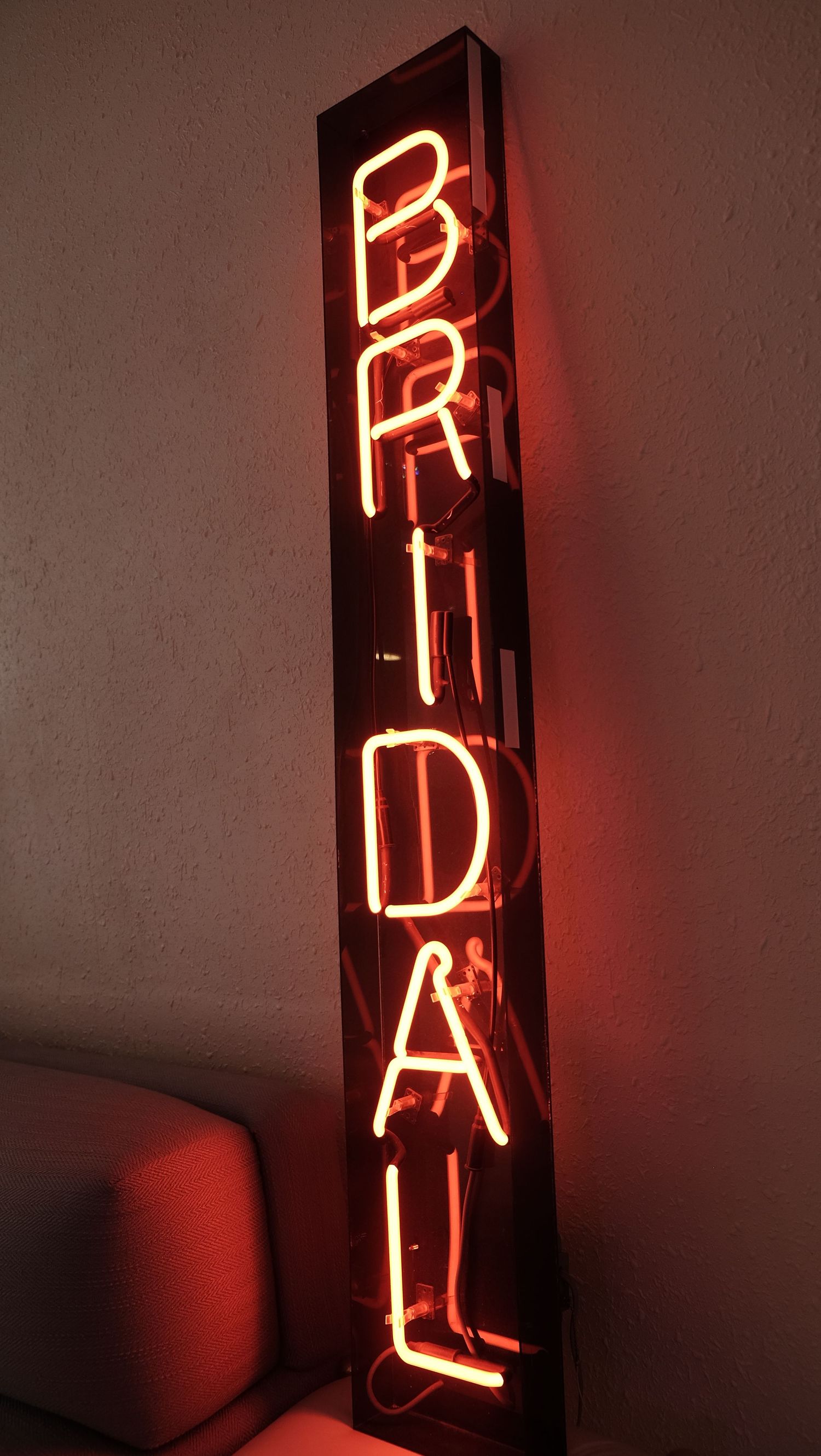Vintage red neon BRIDAL sign glowing against a dark wall, leaning vertically for retro wedding shop decor.