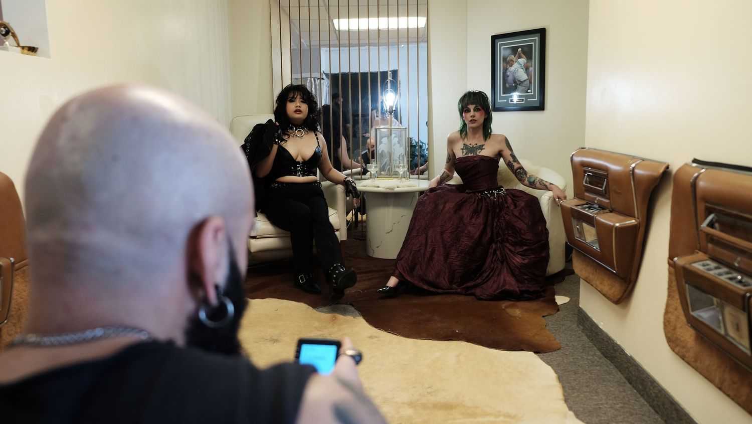 A photographer captures two gothic-styled women posing in a vintage-decorated room with retro furniture.